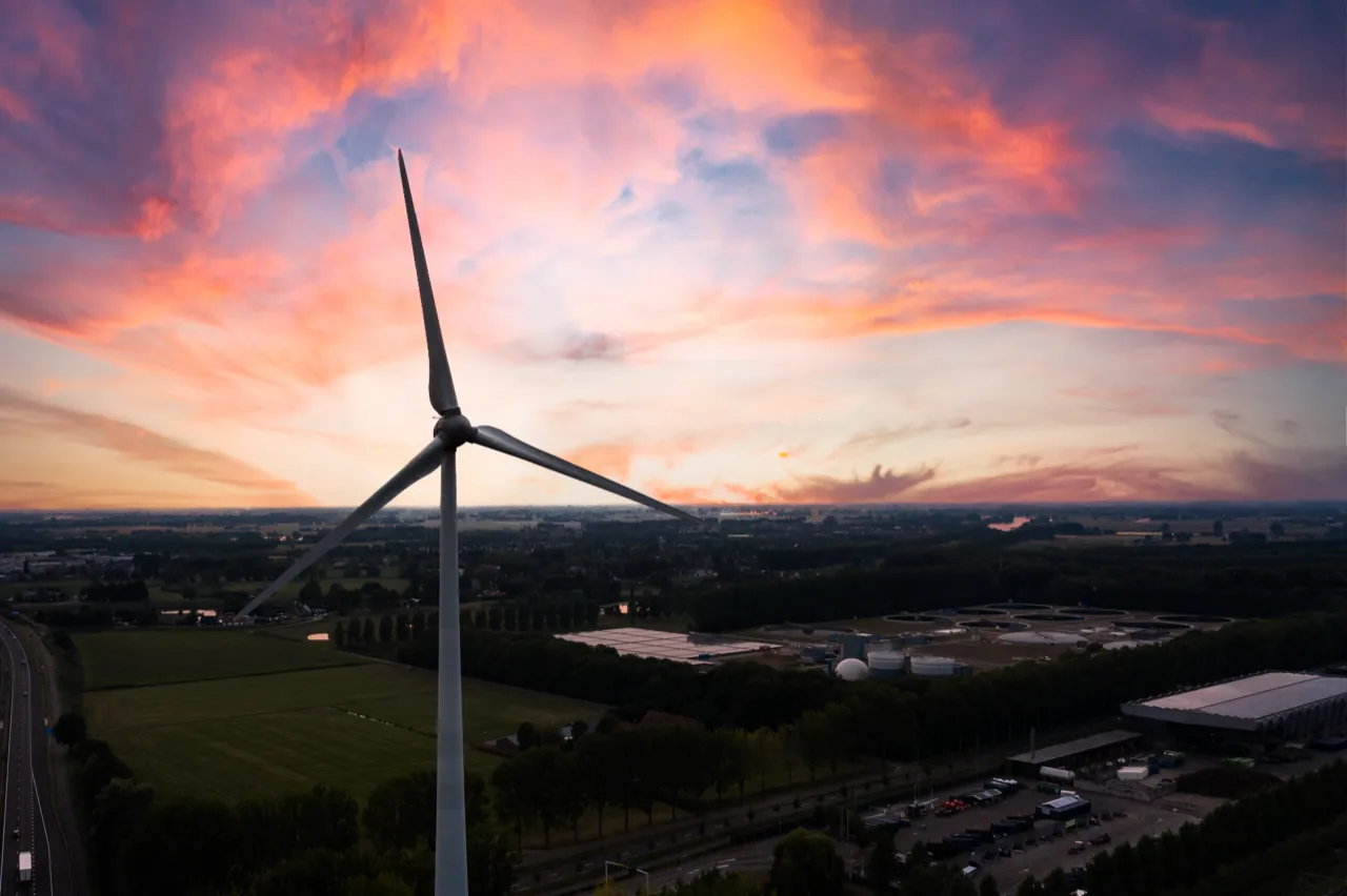 Windturbine bij zonsondergang boven een bedrijventerrein