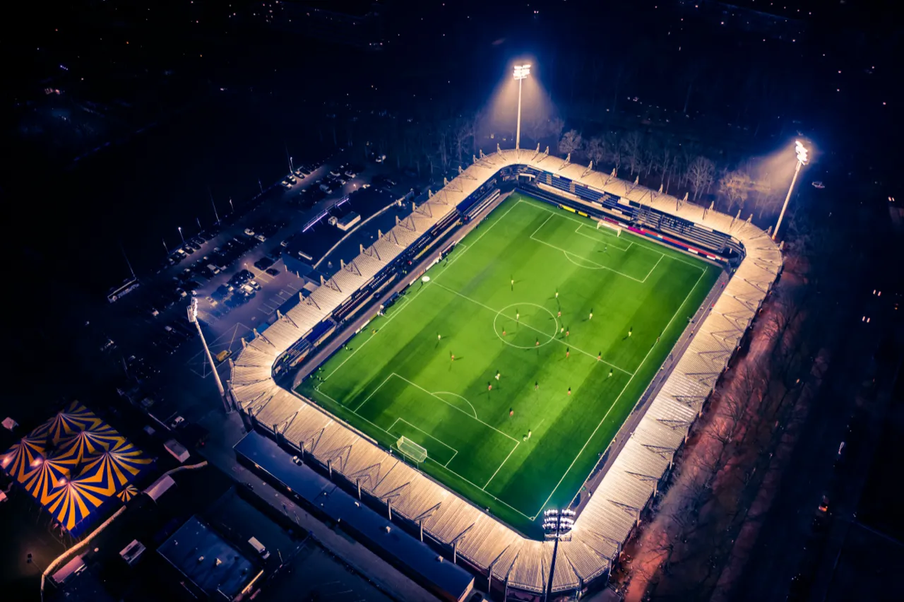 Voetbalstadion tijdens een avondwedstrijd, vanuit de lucht