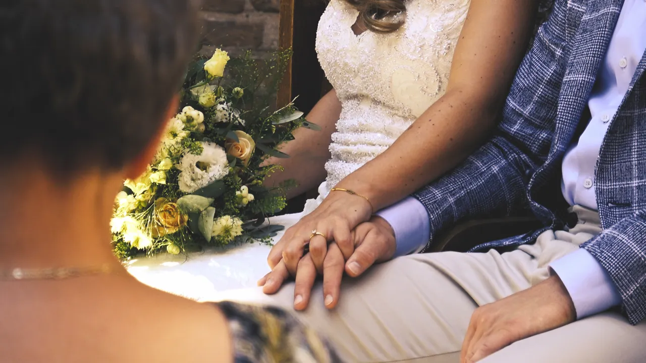 De handen van het bruidspaar met het boeket, tijdens de ceremonie
